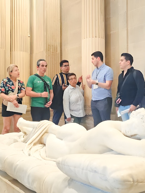 Group of people listening to a guide near a sculpture inside the Louvre Museum, Paris, France.