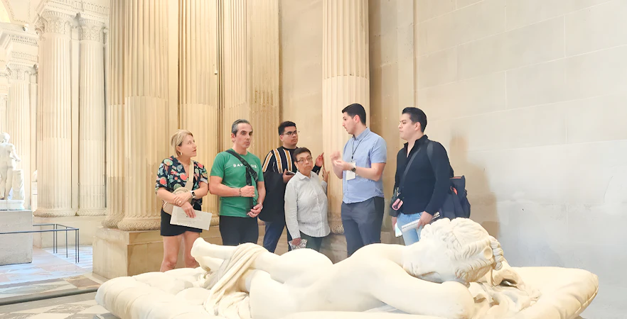 Group of people listening to a guide near a sculpture inside the Louvre Museum, Paris, France.