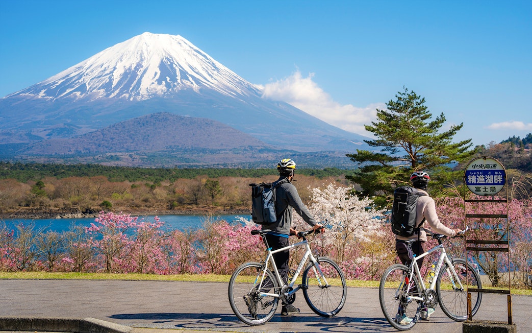 Couple cycling by Lake Yamanaka with Mount Fuji in the background, Japan.