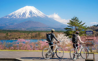 Couple cycling by Lake Yamanaka with Mount Fuji in the background, Japan.