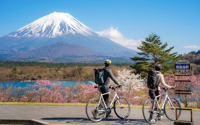 Couple cycling by Lake Yamanaka with Mount Fuji in the background, Japan.