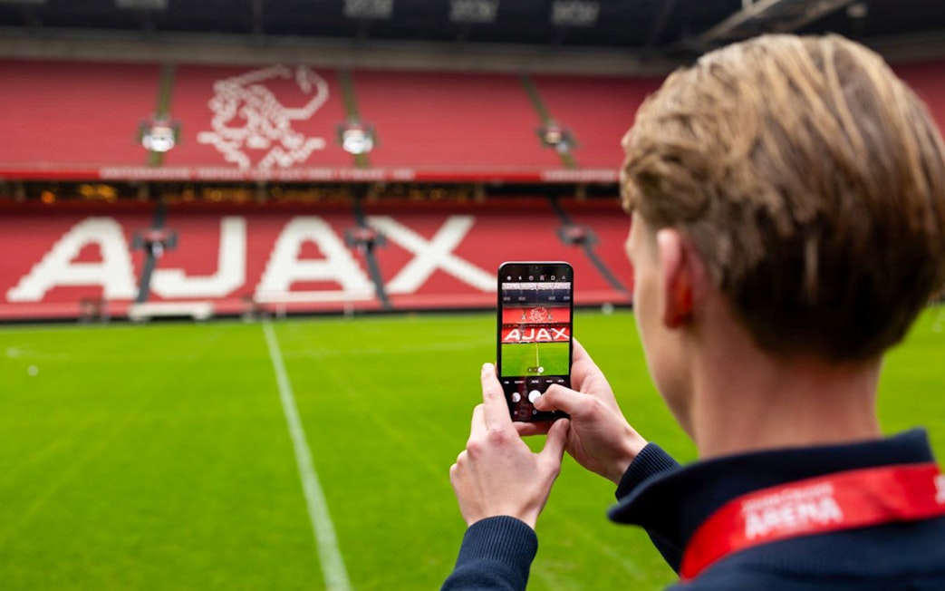 Person photographing Johan Cruijff ArenA field with Ajax logo in Amsterdam.