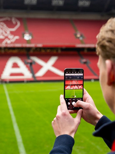 Person photographing Johan Cruijff ArenA field with Ajax logo in Amsterdam.