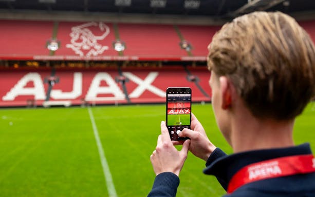 Person photographing Johan Cruijff ArenA field with Ajax logo in Amsterdam.