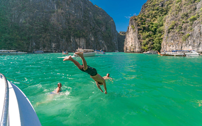Man diving into turquoise water near cliffs on Phi Phi Islands tour, Phuket.
