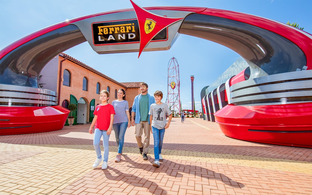 Family walking under Ferrari Land entrance at PortAventura World, with roller coaster in background.