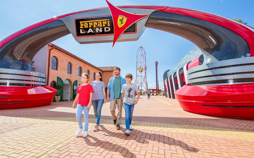 Family walking under Ferrari Land entrance at PortAventura World, with roller coaster in background.