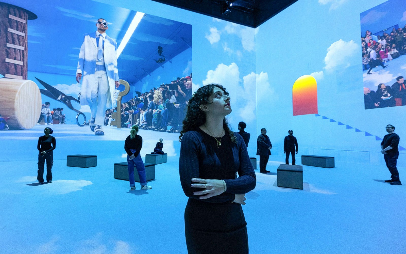 Visitors at Vogue: Inventing the Runway exhibition, observing fashion projections in a blue-lit room.