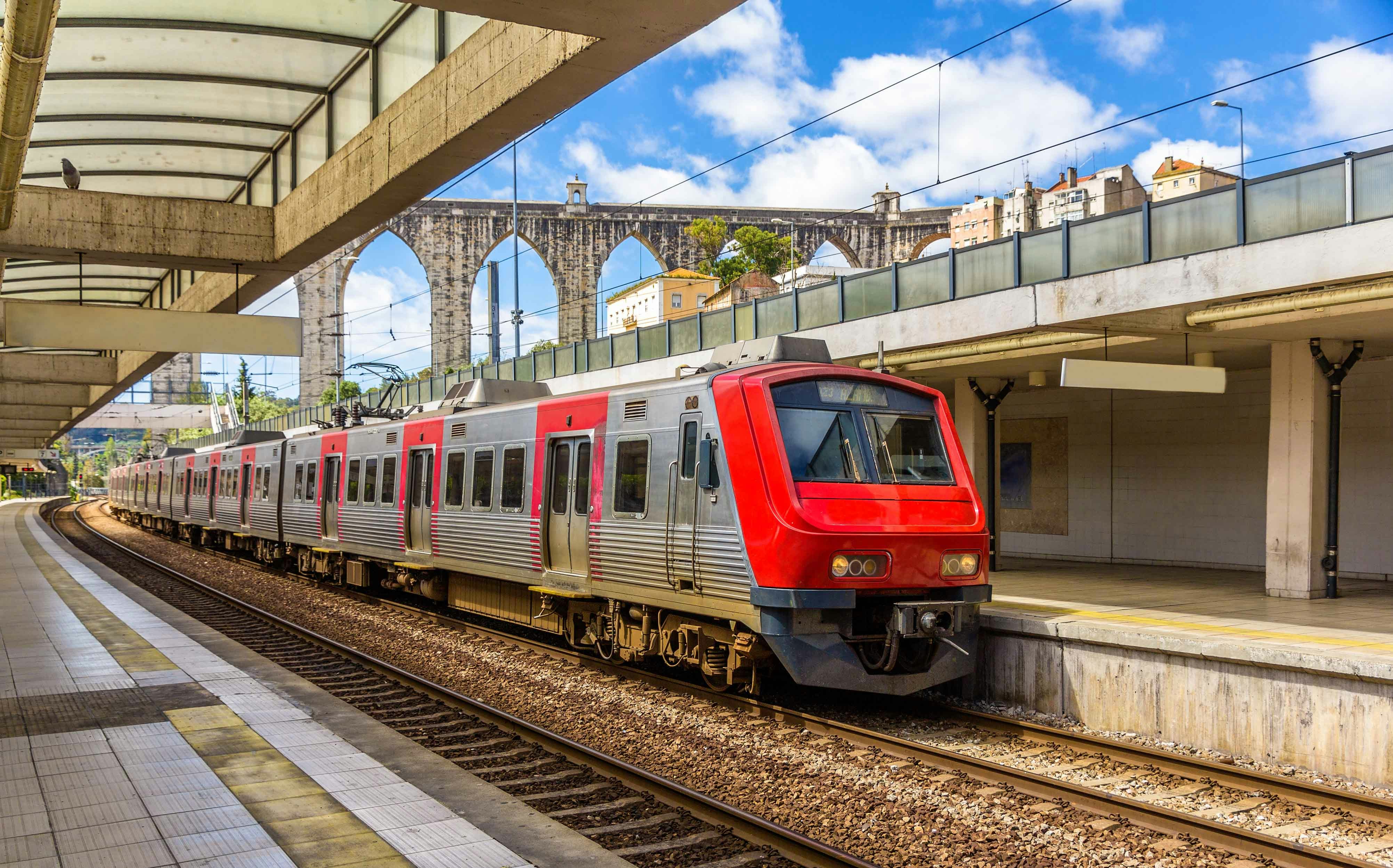 Lisbon train at station with aqueduct in background.