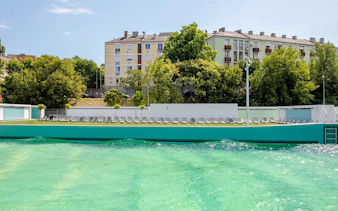 Outdoor pool at Pesterzsebet Bath, Budapest with lounge chairs and surrounding trees.