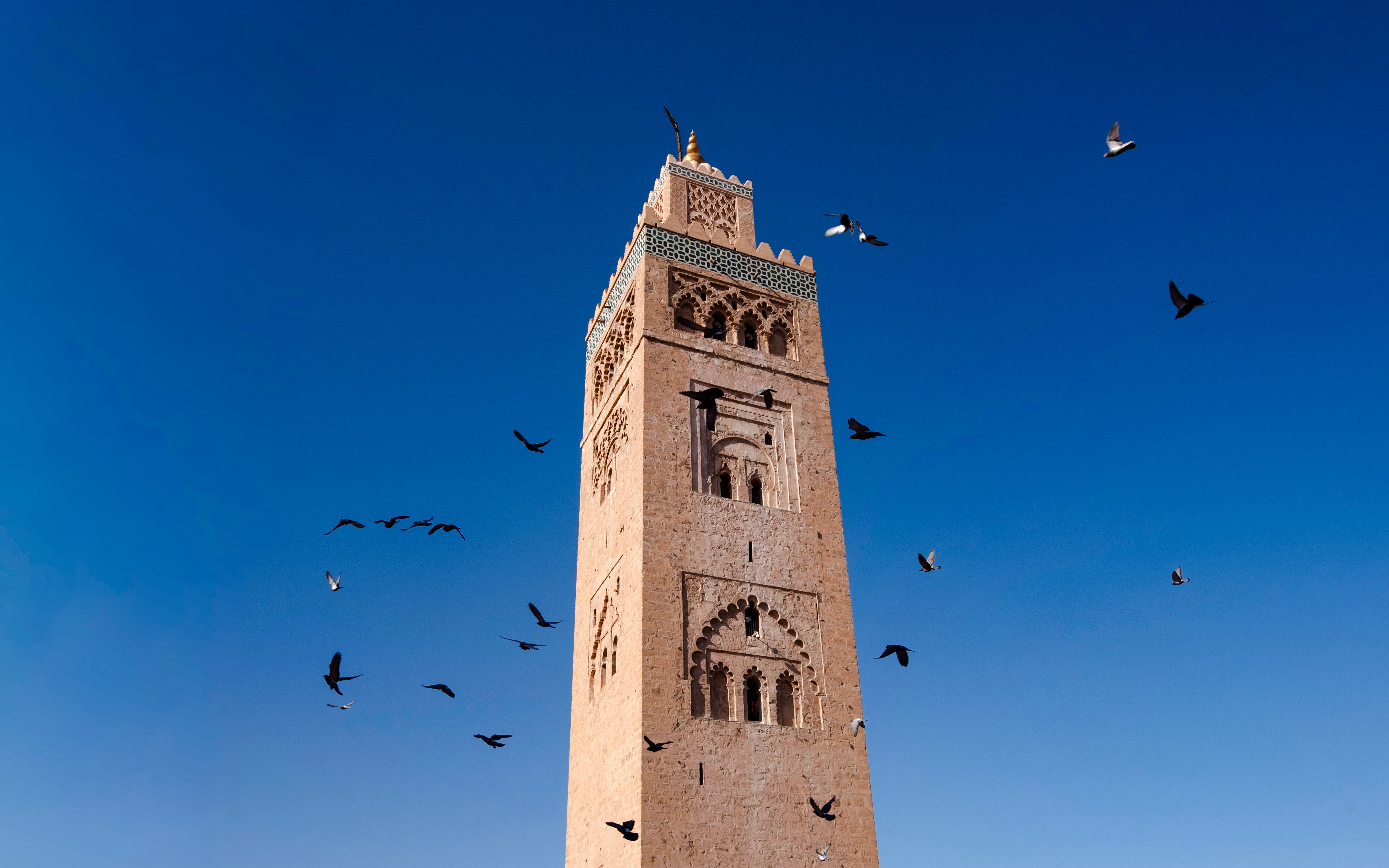 Koutoubia Minaret in Marrakech with birds flying against a clear blue sky.