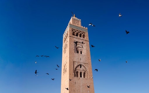 Koutoubia Minaret in Marrakech with birds flying against a clear blue sky.