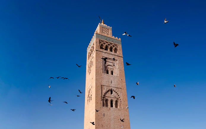 Koutoubia Minaret in Marrakech with birds flying against a clear blue sky.