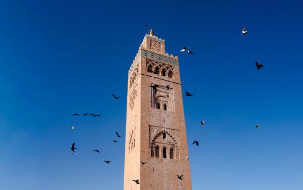 Koutoubia Minaret in Marrakech with birds flying against a clear blue sky.
