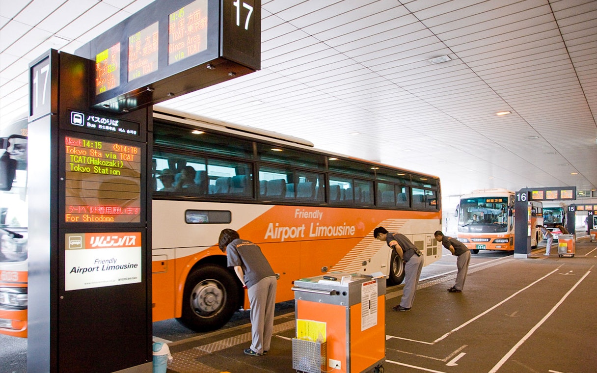 Bus at Narita Airport terminal with staff assisting passengers for transfers to Tokyo and Shinjuku.
