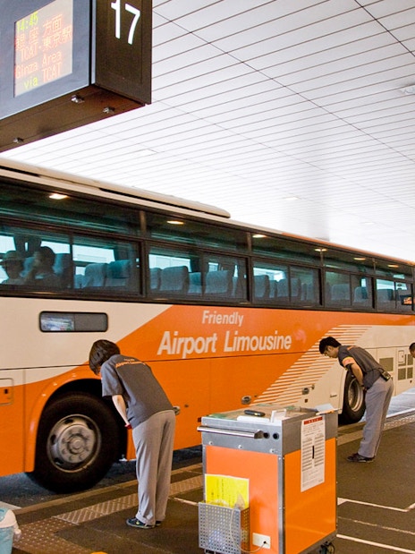 Bus at Narita Airport terminal with staff assisting passengers for transfers to Tokyo and Shinjuku.