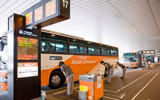 Bus at Narita Airport terminal with staff assisting passengers for transfers to Tokyo and Shinjuku.