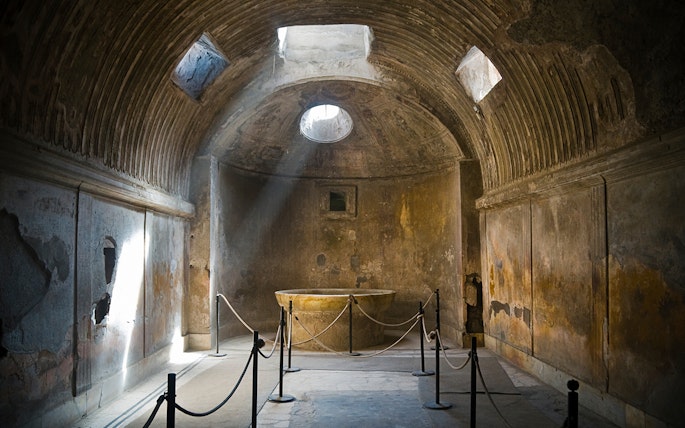 Ancient room in Pompeii with sunlight through ceiling, part of guided tour.