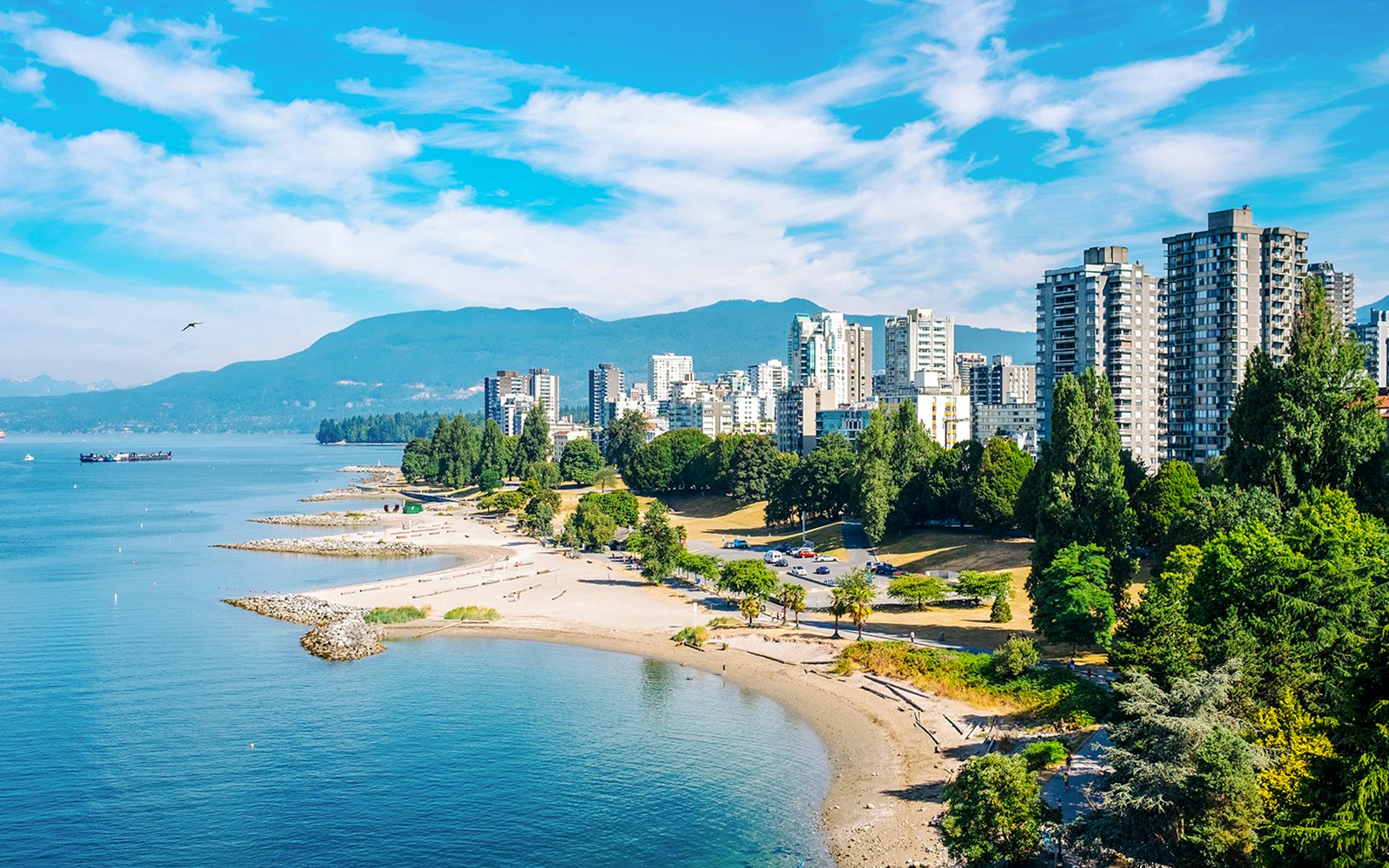 English Bay shoreline with cityscape and mountains in Vancouver, Canada.