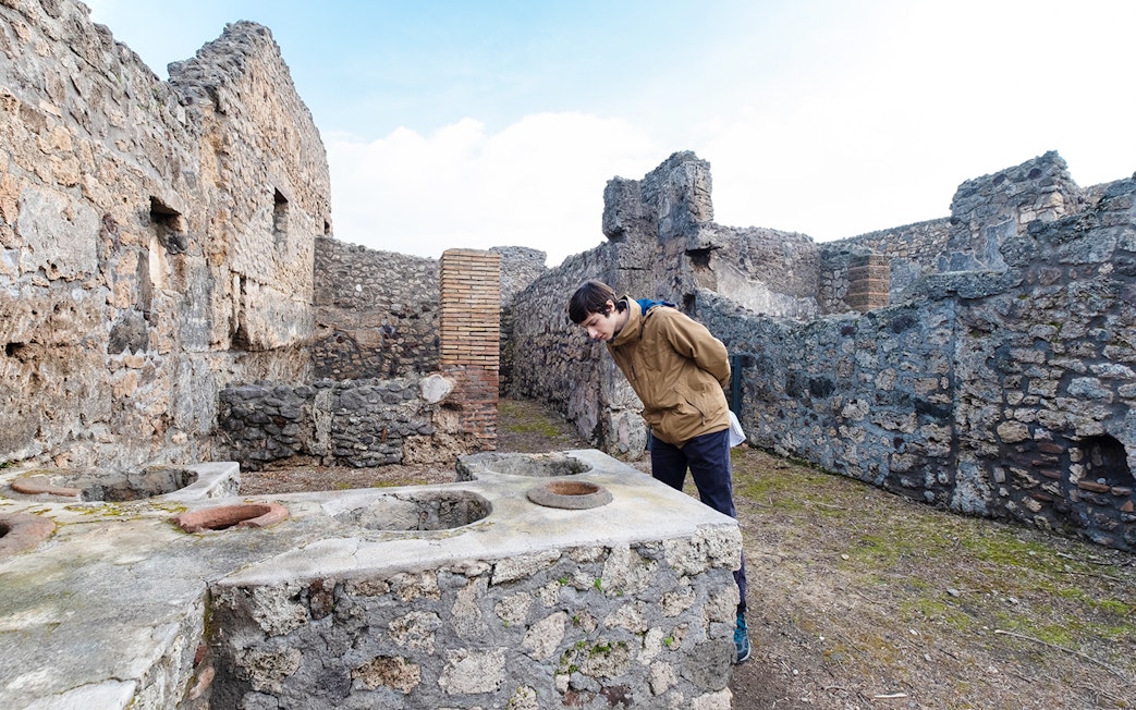 Visitor examining ancient counter at Termopolium in Pompeii ruins.