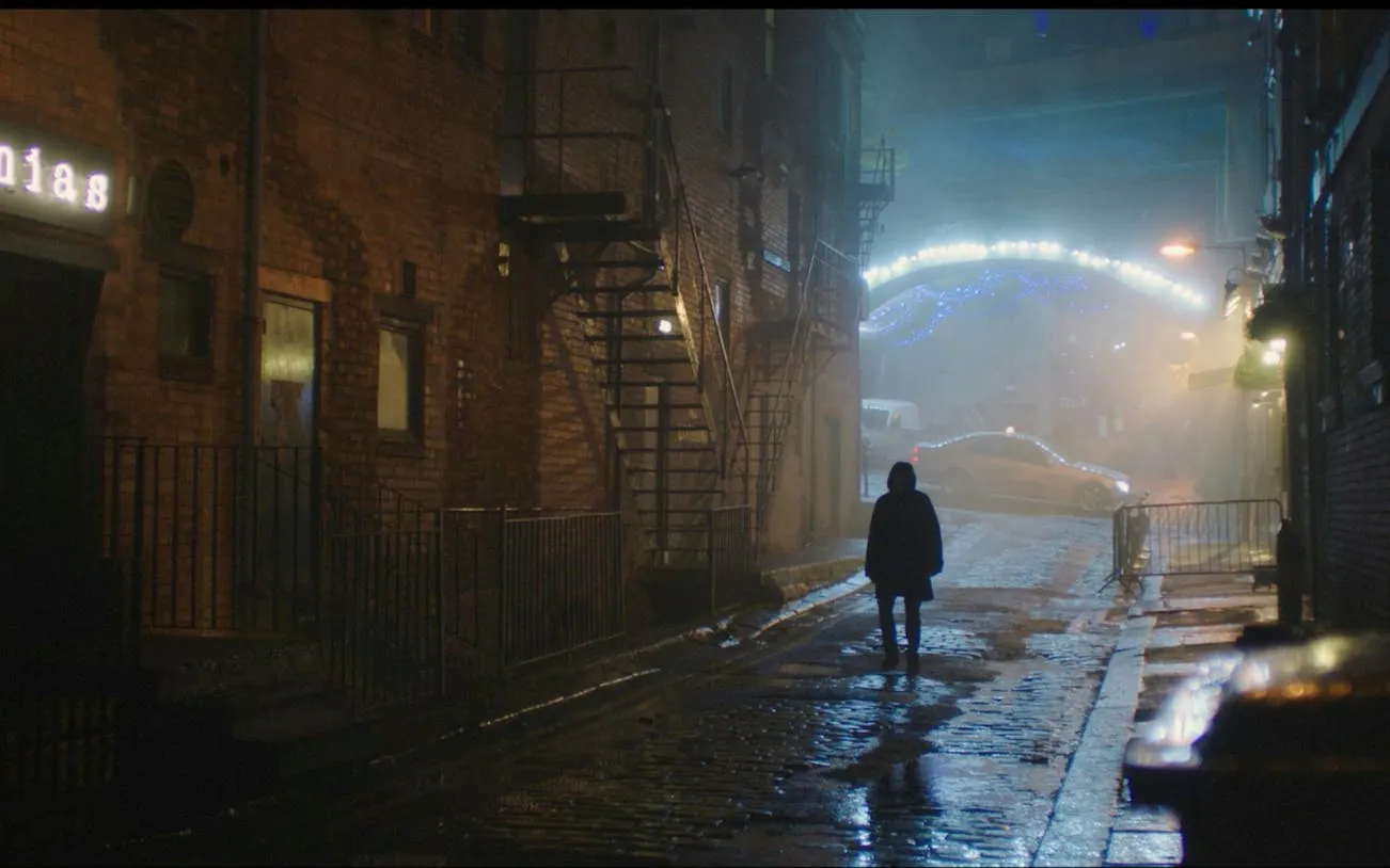 Person walking down a dimly lit cobblestone street in Manchester at night.