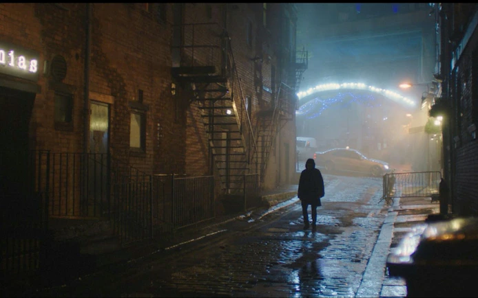 Person walking down a dimly lit cobblestone street in Manchester at night.