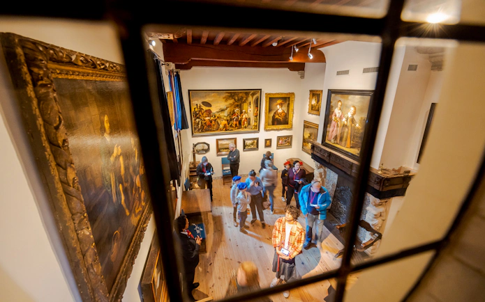 Visitors exploring Rembrandt House Museum in Amsterdam, viewing paintings and exhibits.