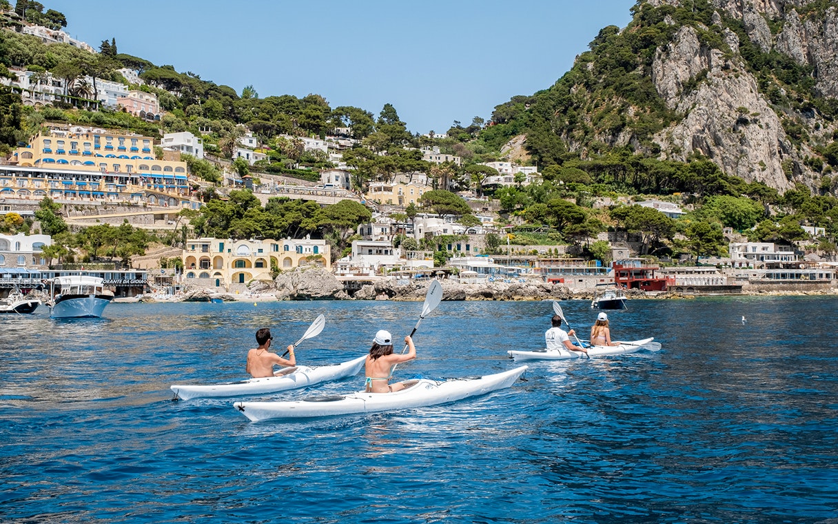 Kayakers paddling near Capri's coastline with colorful buildings and cliffs in the background.