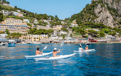 Kayakers paddling near Capri's coastline with colorful buildings and cliffs in the background.