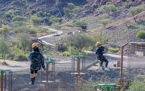 Ziplining adventure at Hatta Wadi Hub with two people on cables over rocky terrain.