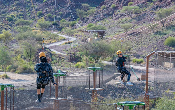 Ziplining adventure at Hatta Wadi Hub with two people on cables over rocky terrain.