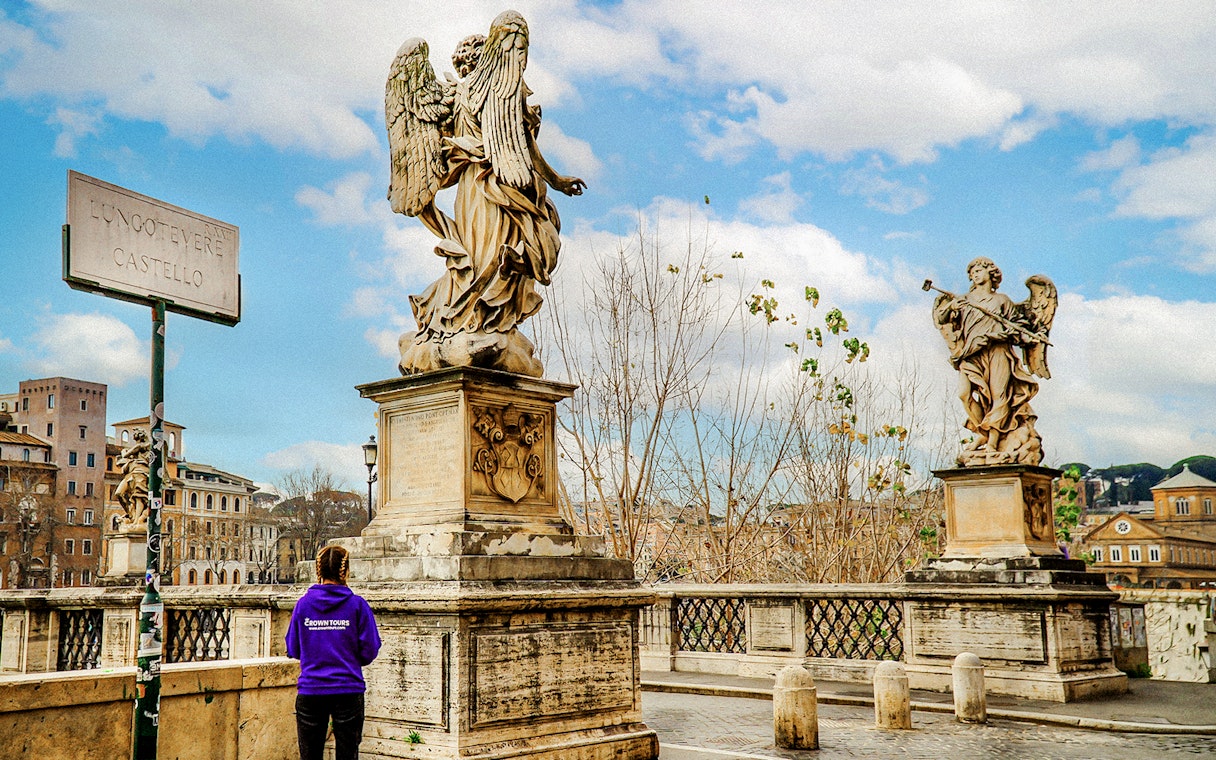 Statues on Ponte Sant'Angelo near Castel Sant'Angelo, Rome, with a tour guide in view.