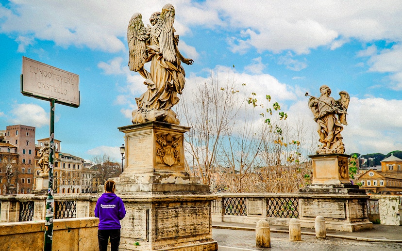 Statues on Ponte Sant'Angelo near Castel Sant'Angelo, Rome, with a tour guide in view.