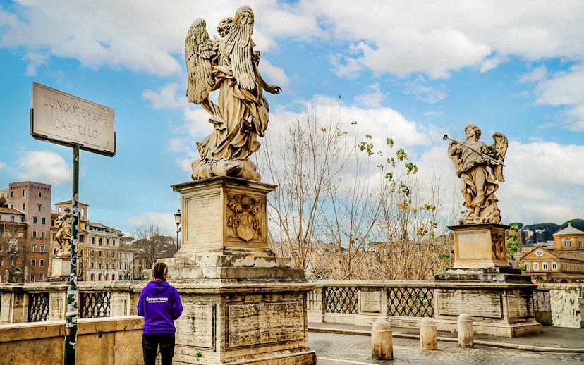 Statues on Ponte Sant'Angelo near Castel Sant'Angelo, Rome, with a tour guide in view.