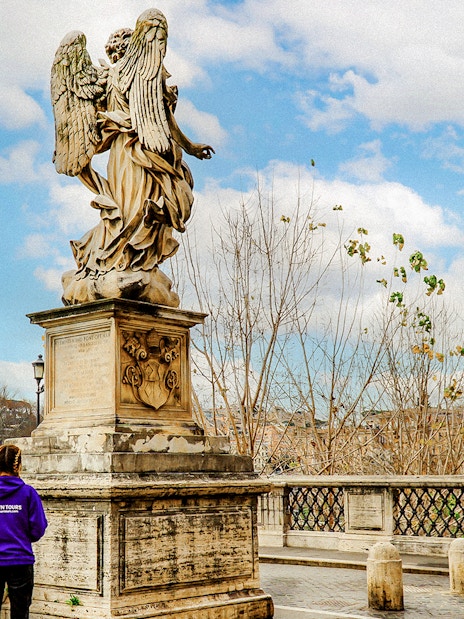 Statues on Ponte Sant'Angelo near Castel Sant'Angelo, Rome, with a tour guide in view.