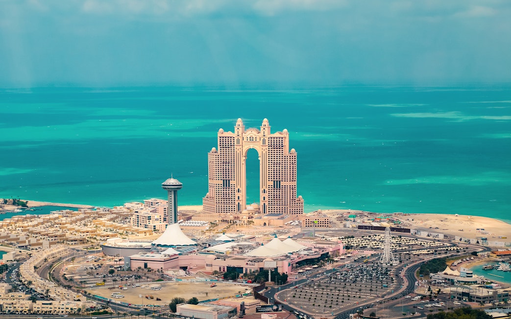 Aerial view of Abu Dhabi skyline with Etihad Towers and turquoise sea.