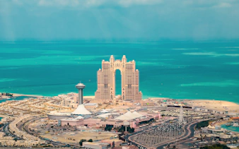 Aerial view of Abu Dhabi skyline with Etihad Towers and turquoise sea.