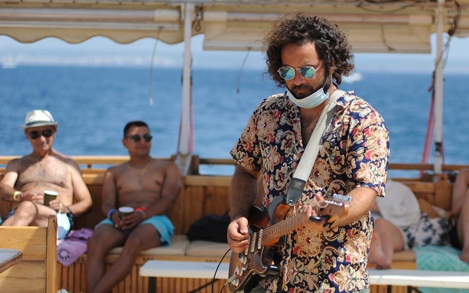 Tourist playing guitar on catamaran boat with ocean view.