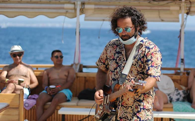 Tourist playing guitar on catamaran boat with ocean view.
