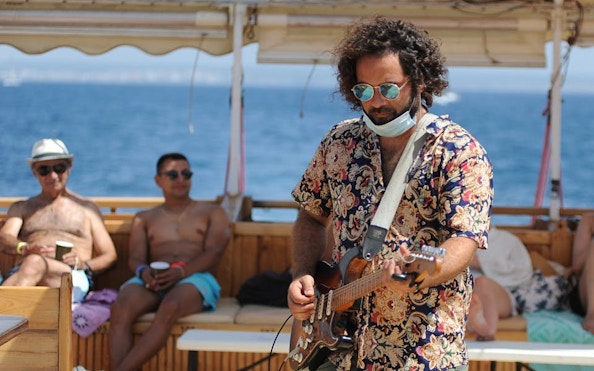 Tourist playing guitar on catamaran boat with ocean view.