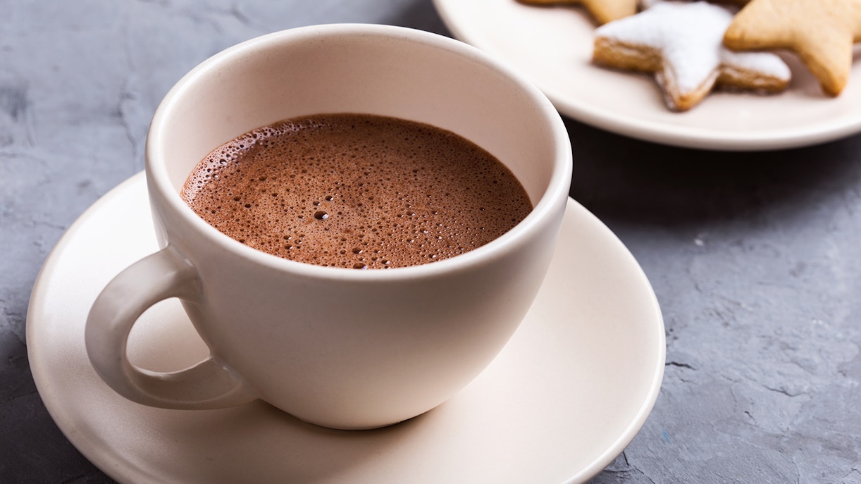 Hot chocolate in a white cup with star-shaped cookies on a plate.