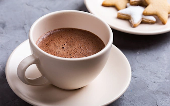Hot chocolate in a white cup with star-shaped cookies on a plate.