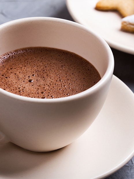 Hot chocolate in a white cup with star-shaped cookies on a plate.