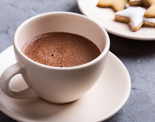 Hot chocolate in a white cup with star-shaped cookies on a plate.