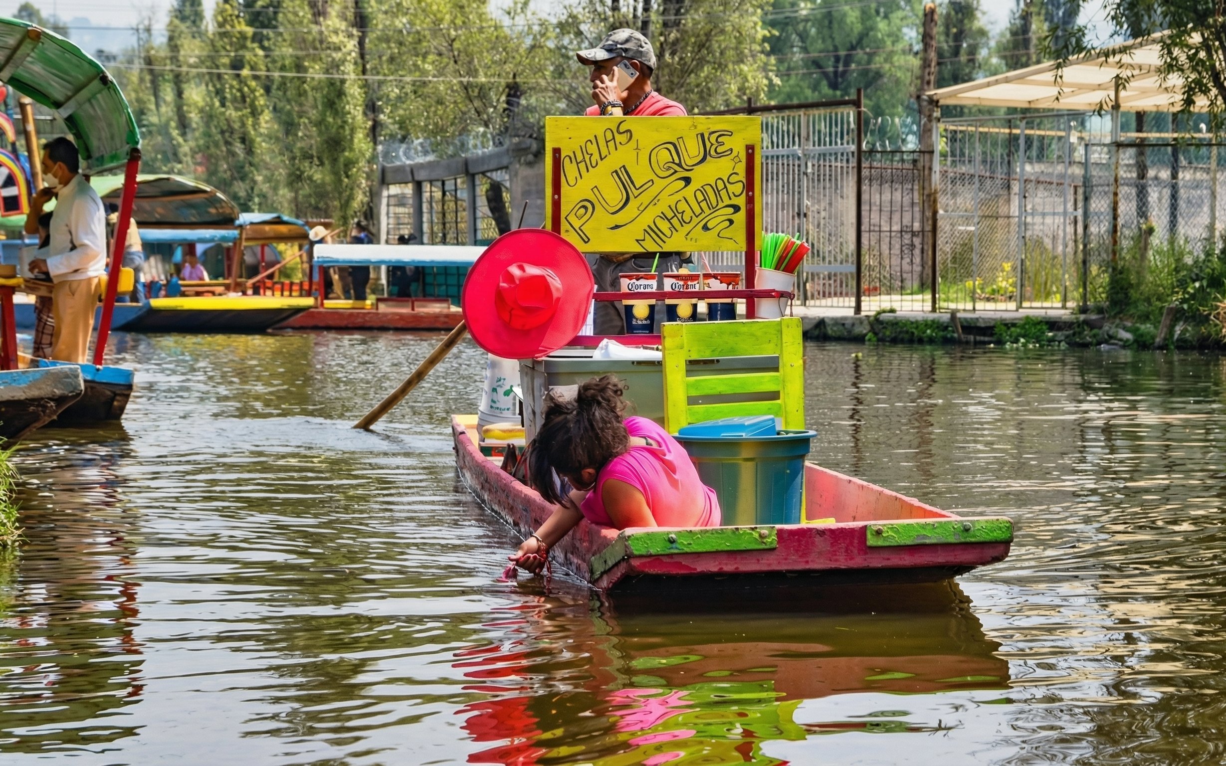 Colorful boat on Xochimilco canal with vendor and passenger enjoying the water.