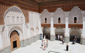 Ben Youssef Medersa courtyard with intricate carvings and visitors, Marrakech.