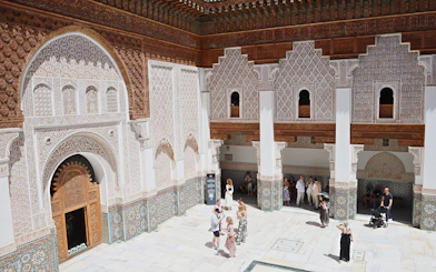 Ben Youssef Medersa courtyard with intricate carvings and visitors, Marrakech.