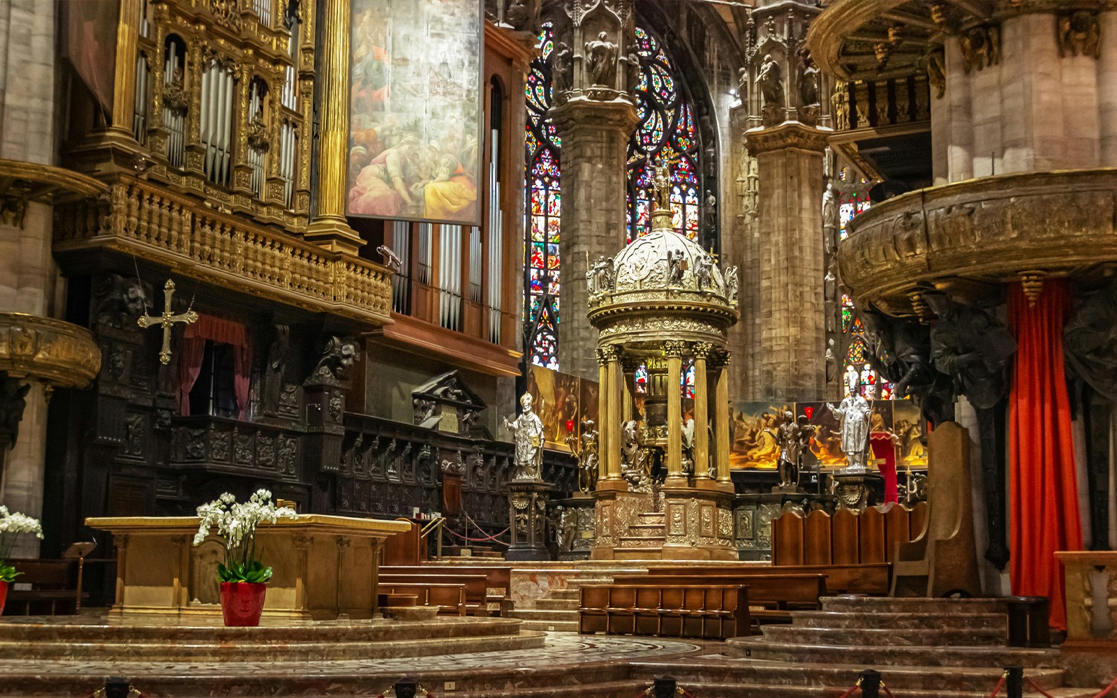 Presbytery and altar inside Duomo di Milano with ornate carvings and stained glass windows.