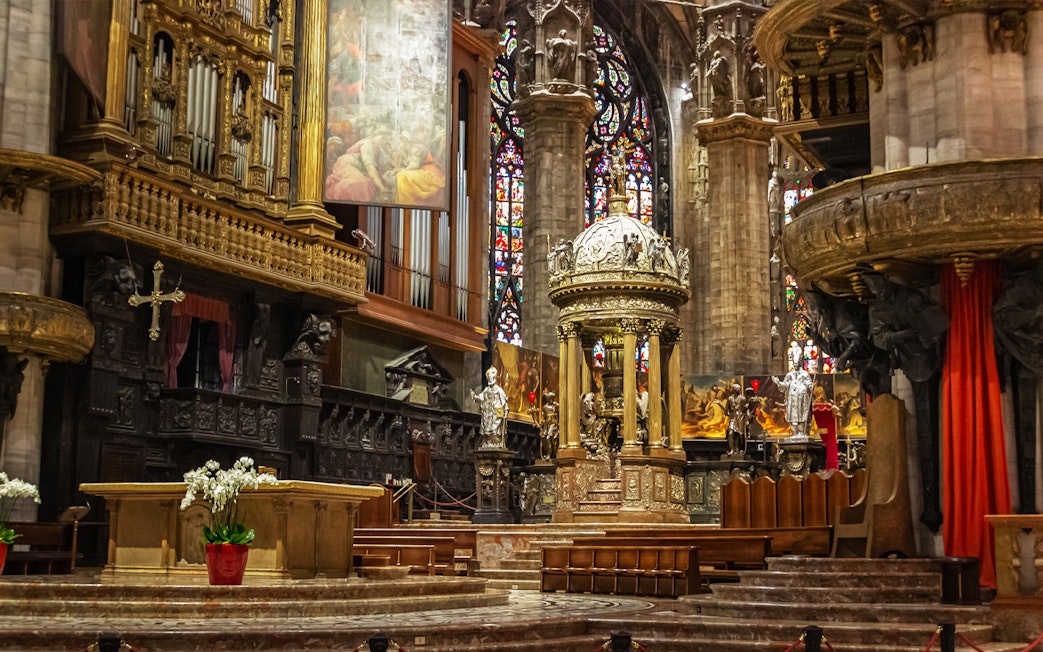 Presbytery and altar inside Duomo di Milano with ornate carvings and stained glass windows.