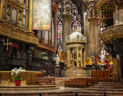 Presbytery and altar inside Duomo di Milano with ornate carvings and stained glass windows.